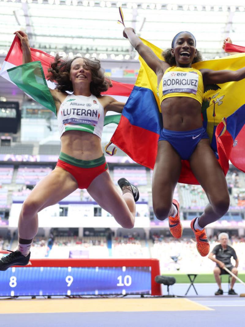 Three female athletes hold their flags and jump to celebrate 