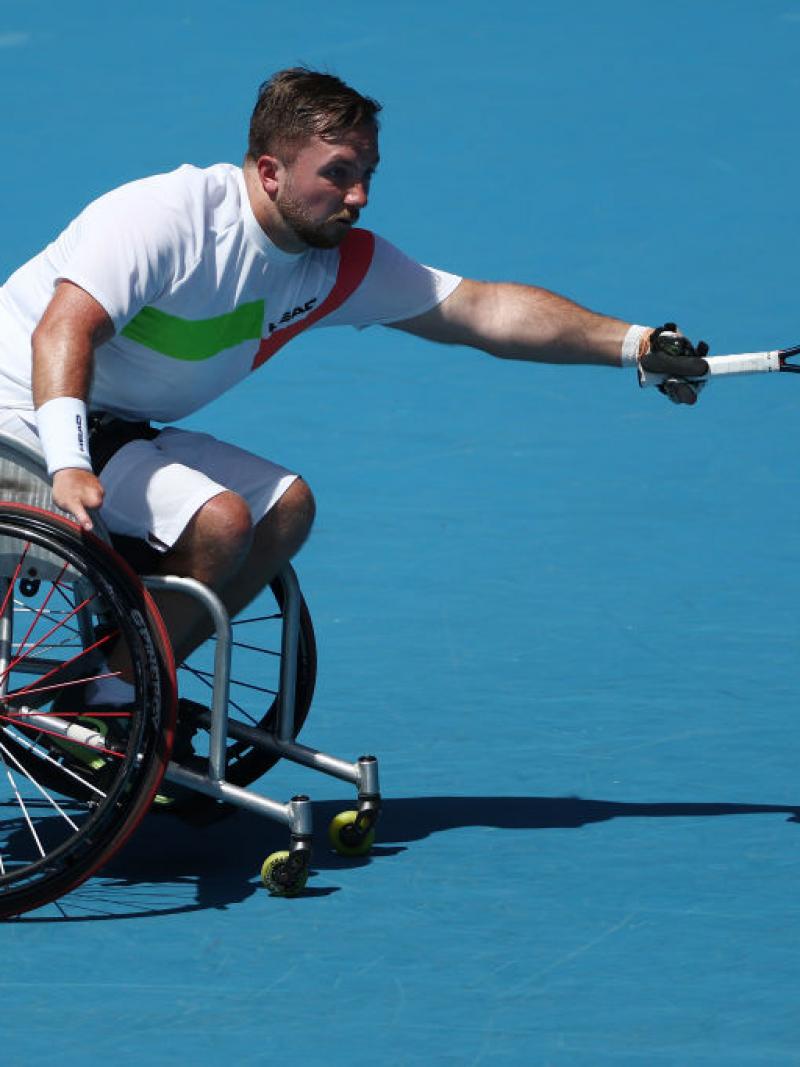 A male wheelchair tennis player reaches to return a shot