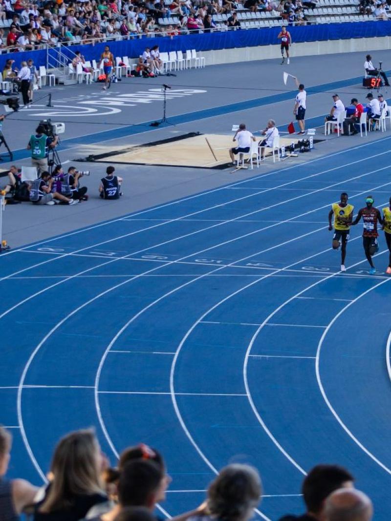 A group of men running with guides in an athletics stadium