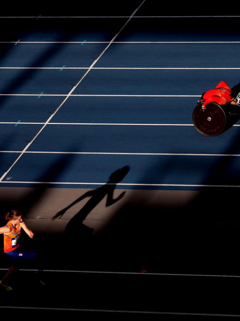 A female athlete with prosthetic legs jumping next to a wheelchair racer in the track