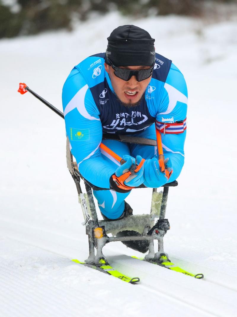 A male sit-skiing athlete wearing a blue skiing suit is competing at the Para Biathlon World Championships