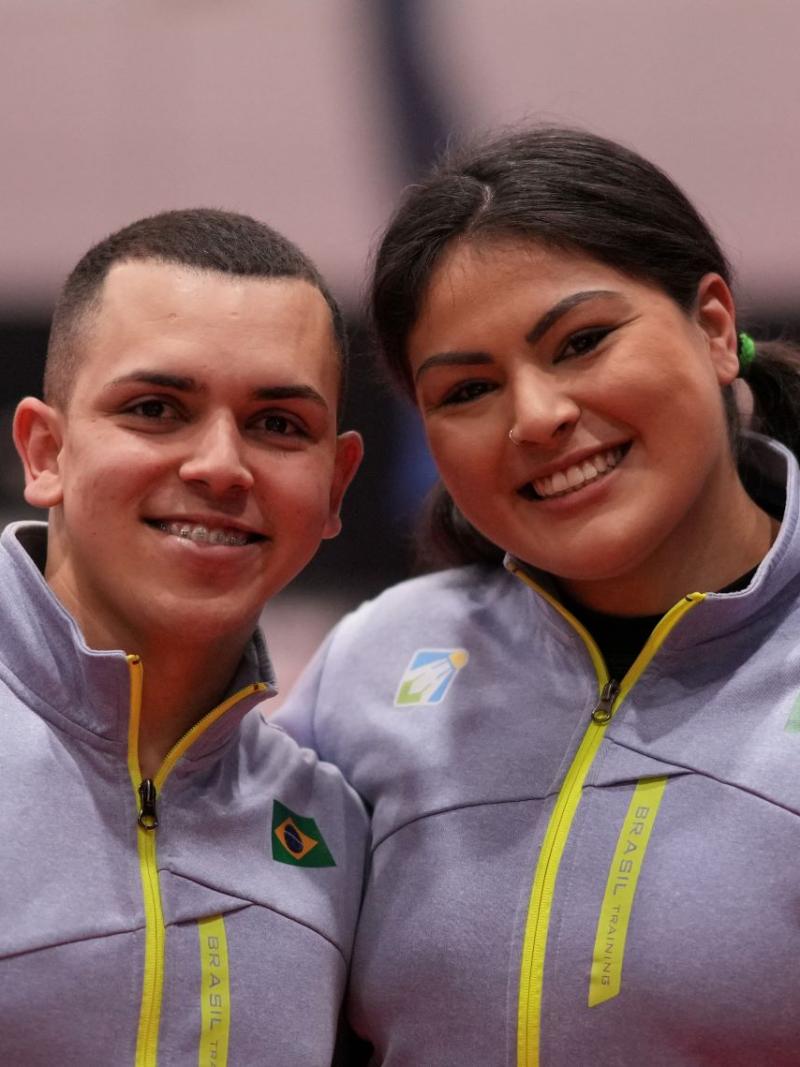 A male athlete and a female athlete pose for a photo together. They are wearing Brazil's gray jersey