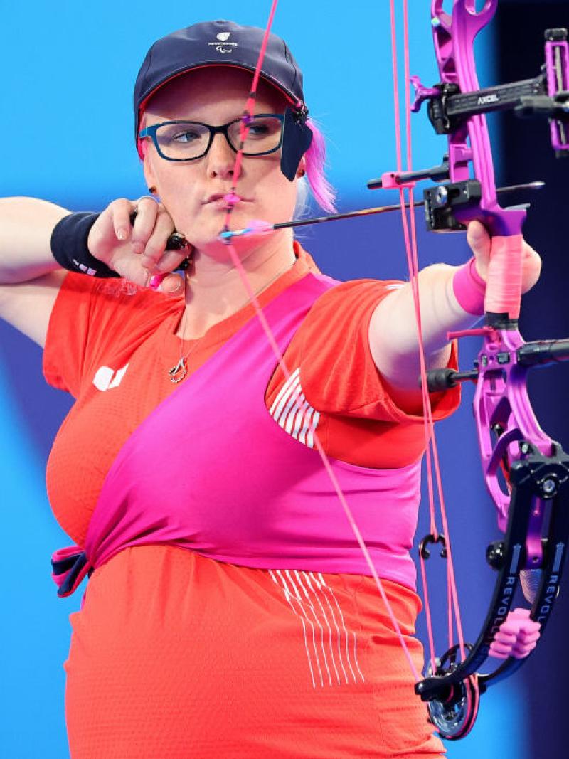 A female Para archer who is wearing a red T-shirt is aiming her bow while seven months pregnant