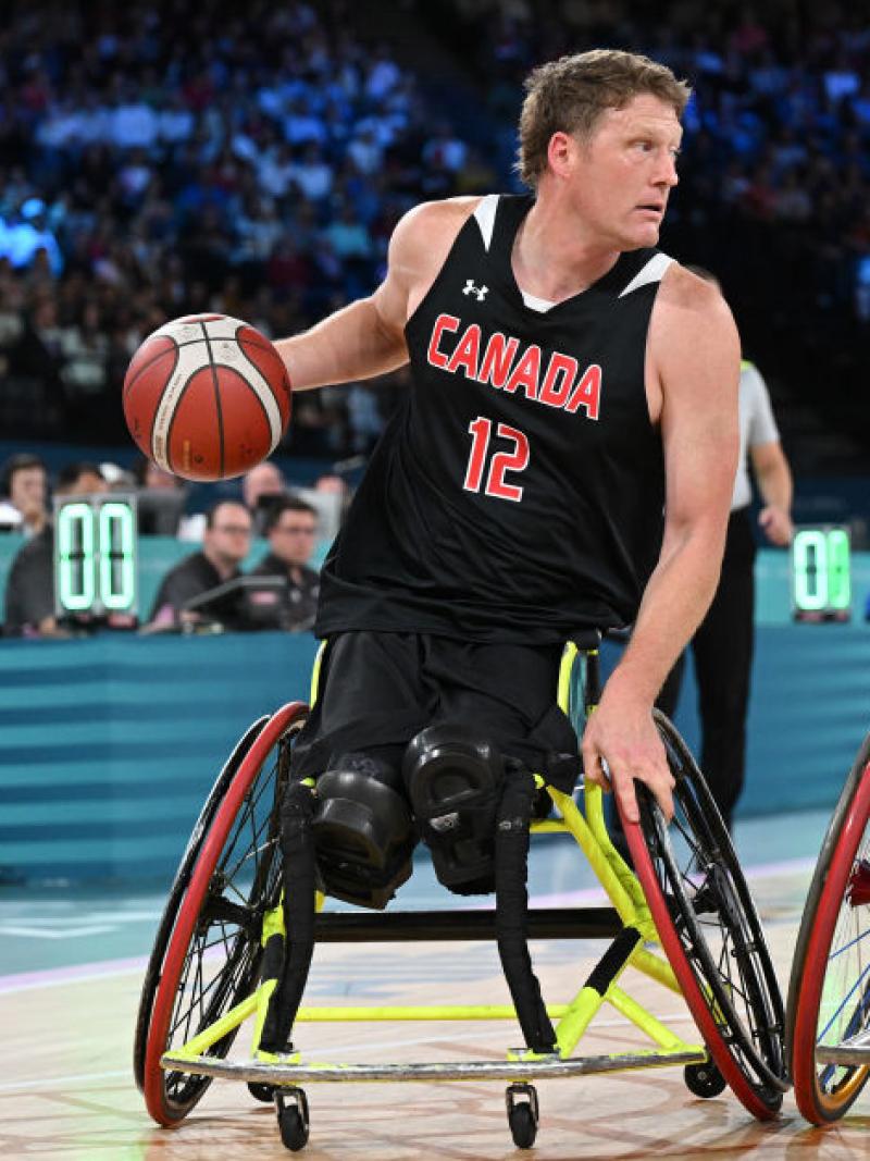 Two male wheelchair basketball players in action. The player in the left is dribbling the ball