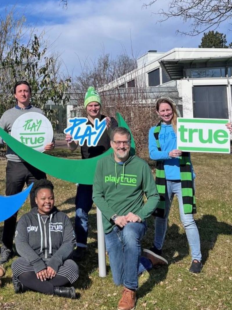 Seven people holding banners that read Play True in front of the IPC headquarters