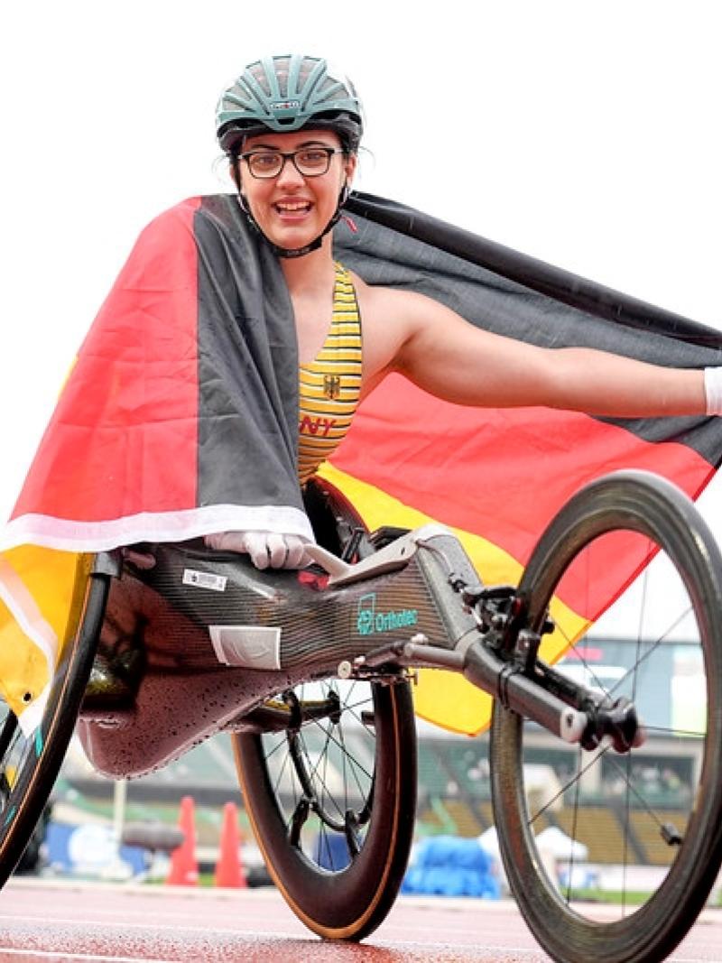 A female wheelchair racer celebrates on the track, holding the German flag