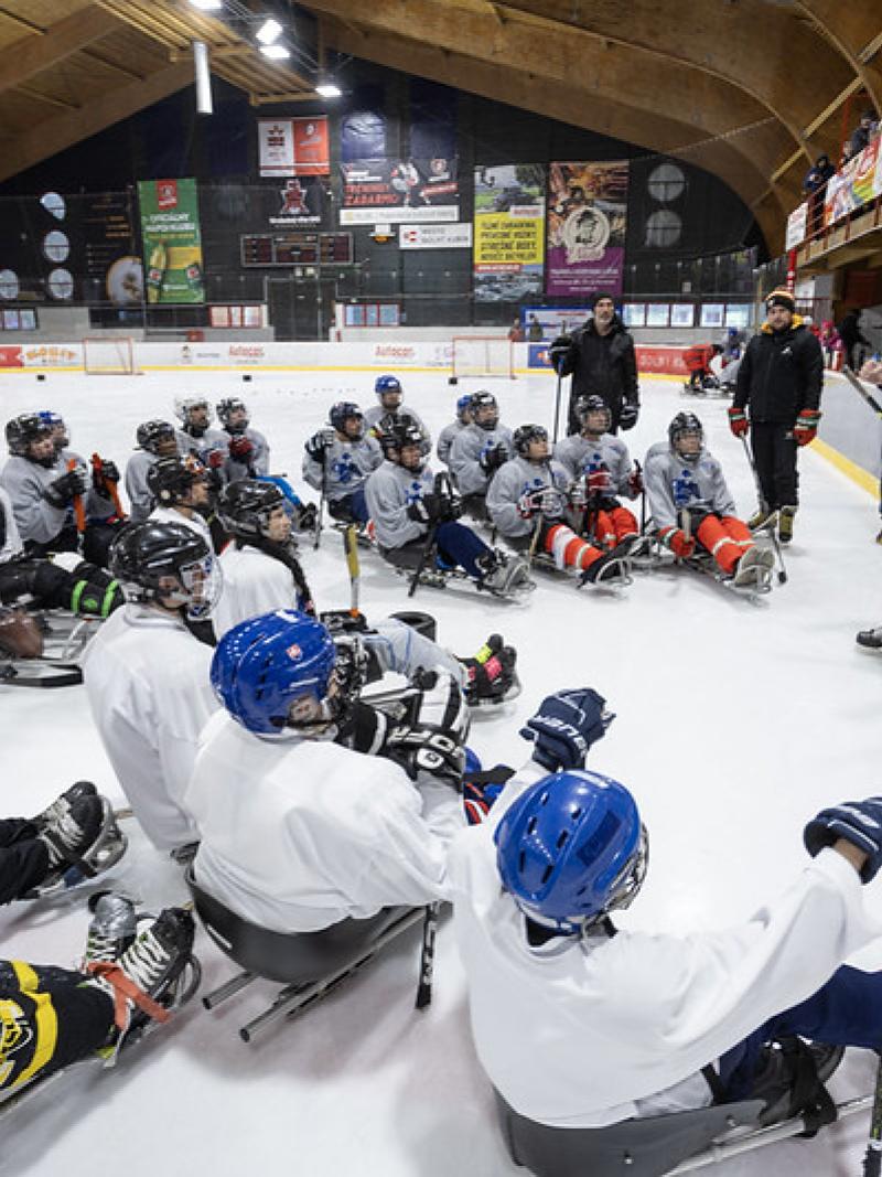 About four officials speaking in front of a group of Para ice hockey players