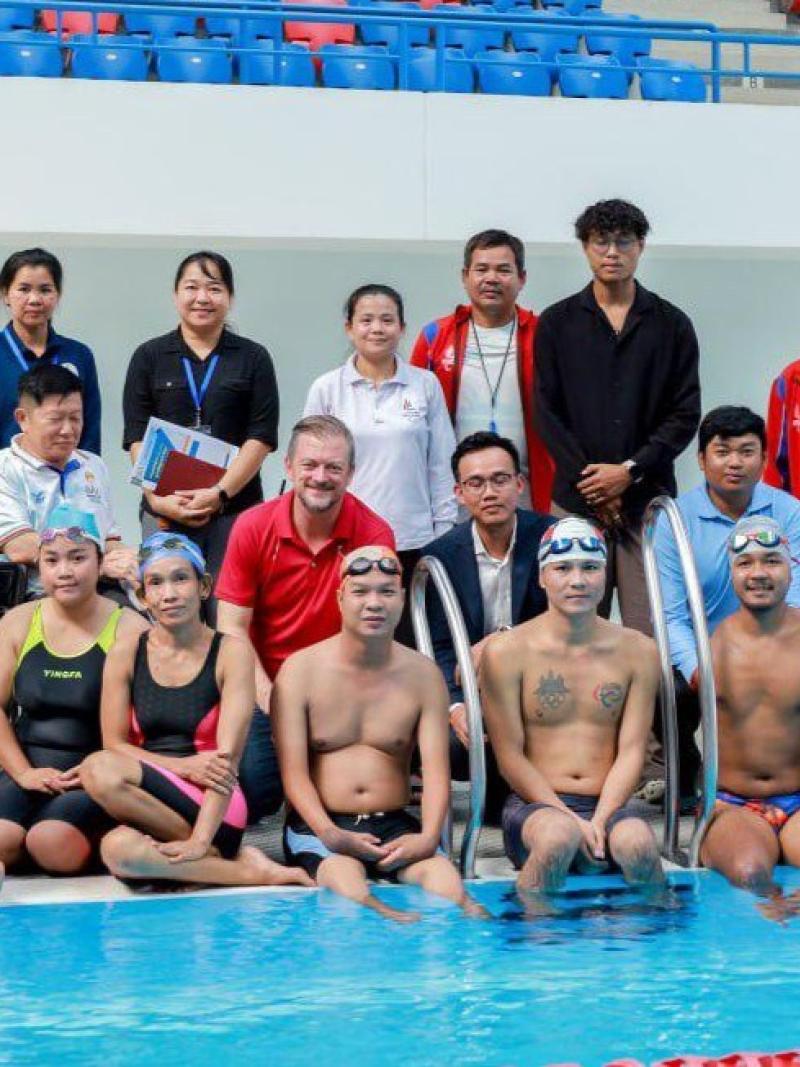 A group photo of about 20 people including swimmers and officials by the pool