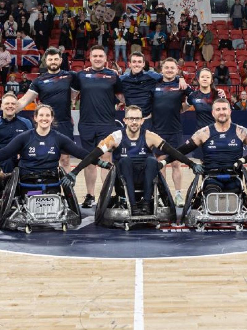 Seventeen people, including wheelchair rugby players and staff, pose for a group photo on a court