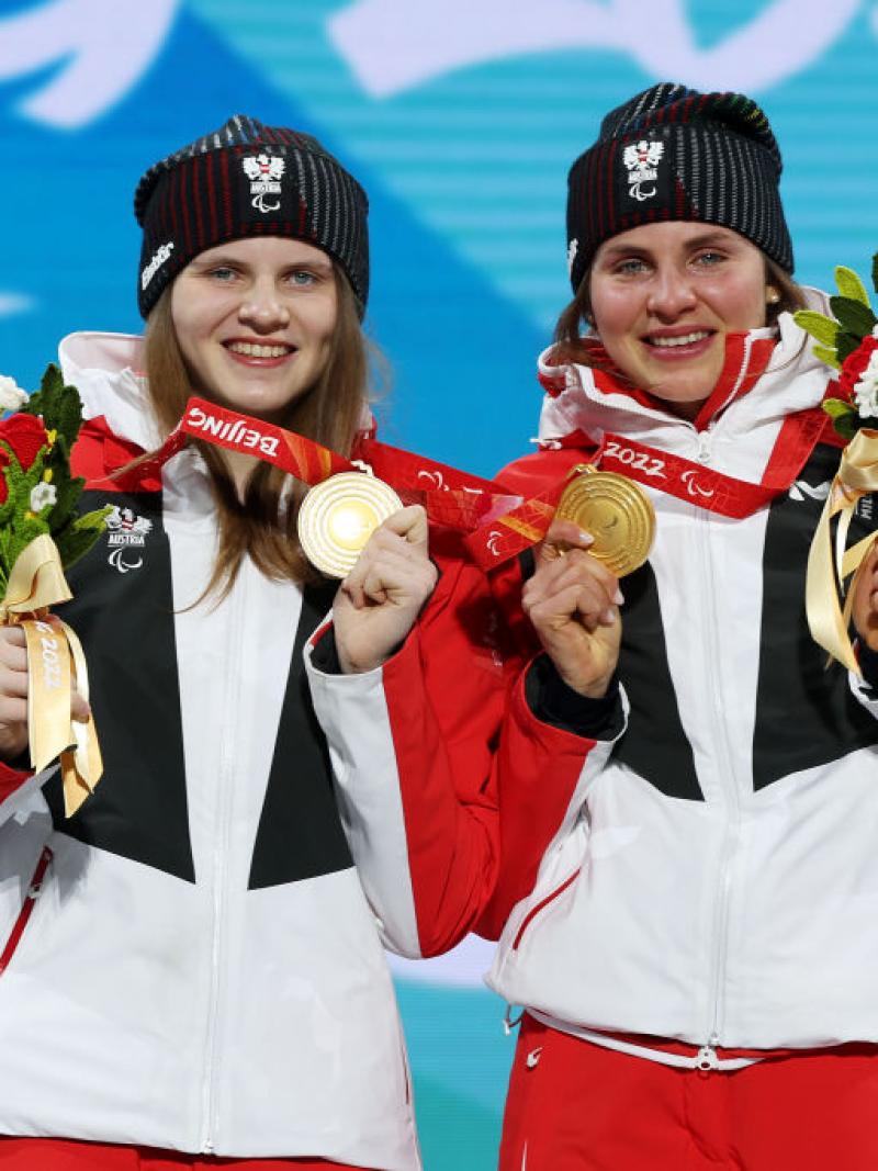 Two female athletes posing for a picture on the podium after receiving gold medals