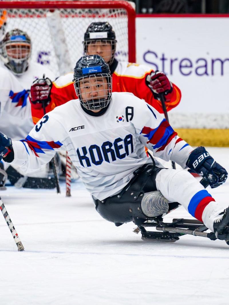A Korean Para ice hockey player watched by three other players on ice