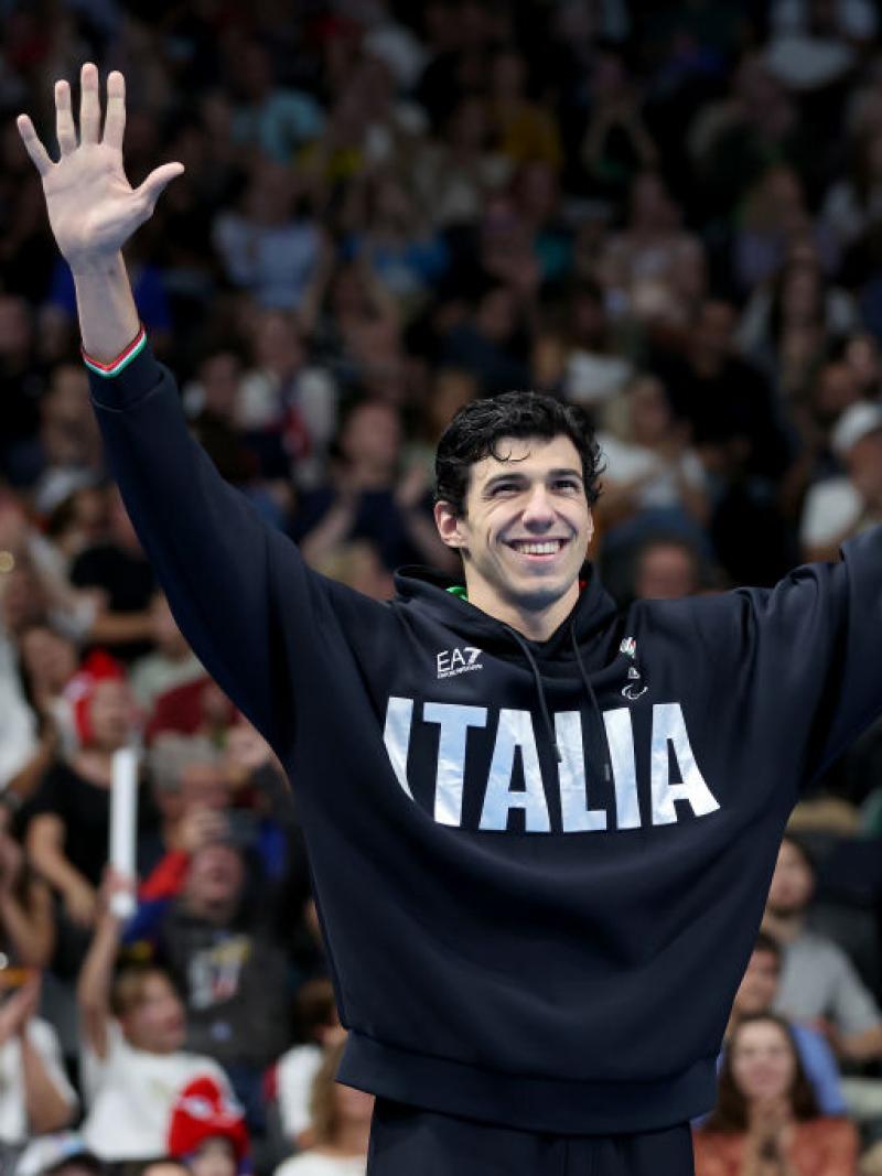 A male Para swimmer wearing a hoodie that says Italia raises his arms in front of a crowd