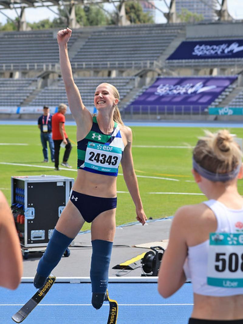 A female athlete with prosthetic legs waving from a track