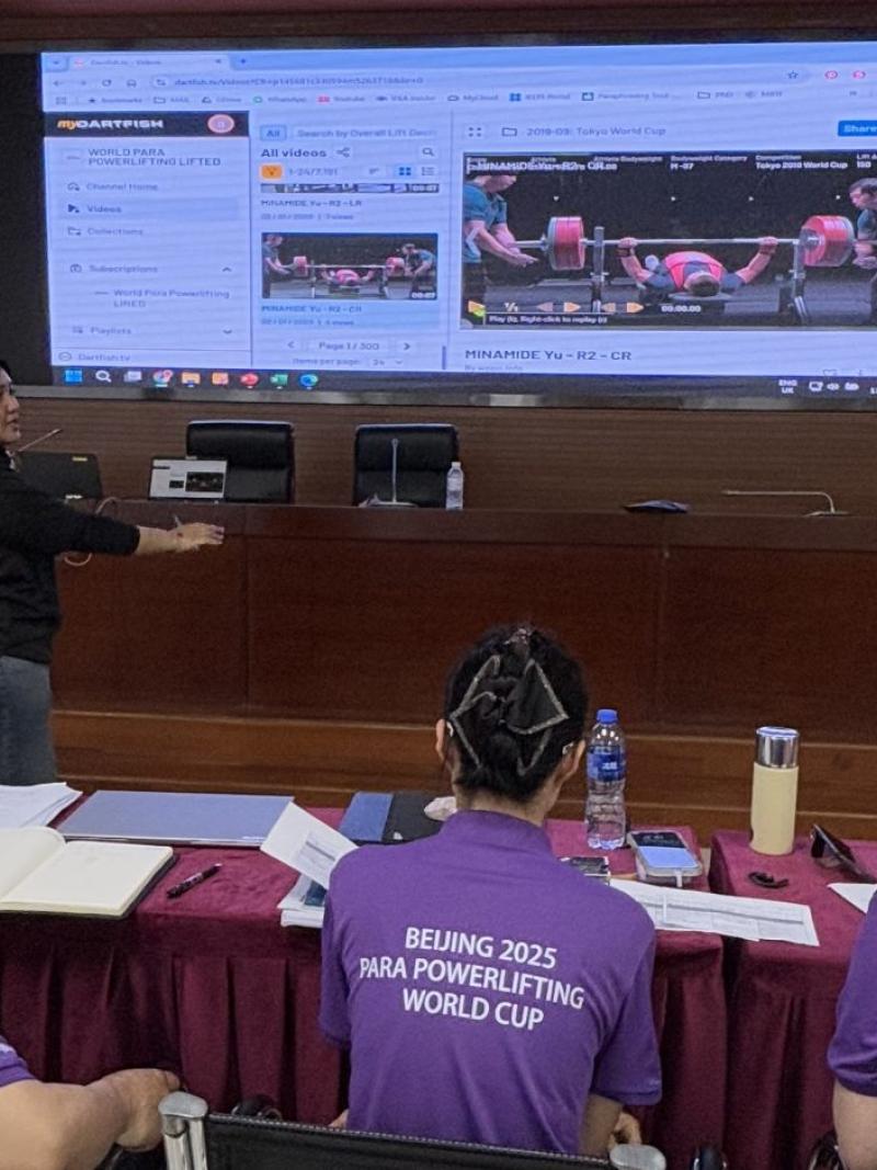 Three participants watching a woman make a presentation on a screen