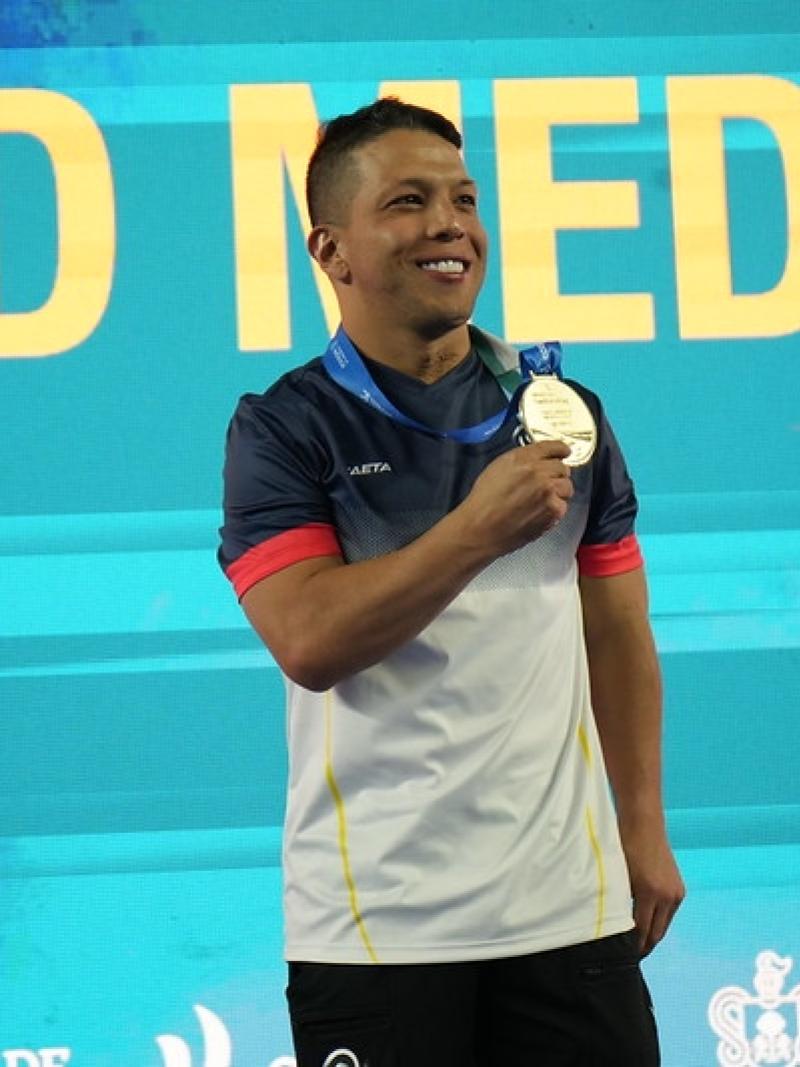 A man showing his medal with a backdrop with the words gold medal behind him