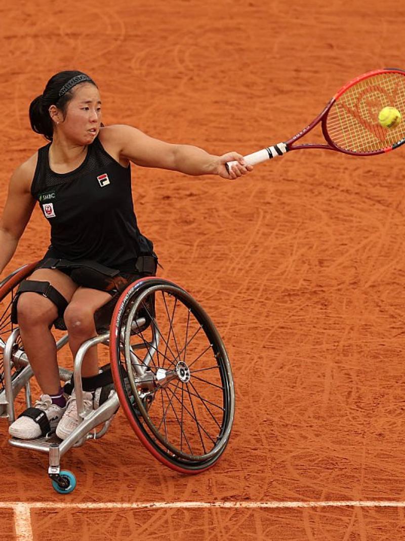 A female wheelchair tennis player plays a forehand on red clay court