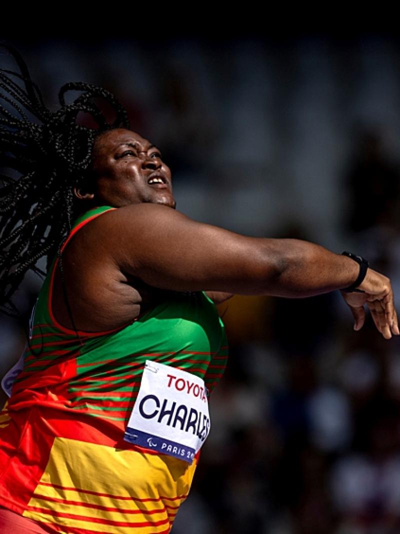A female athlete wearing a red, yellow and green uniform is throwing