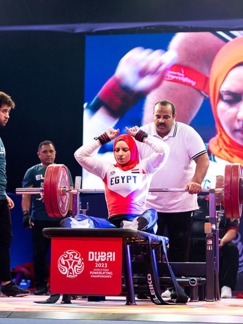 A female powerlifter on the bench observed by the coach and three loaders