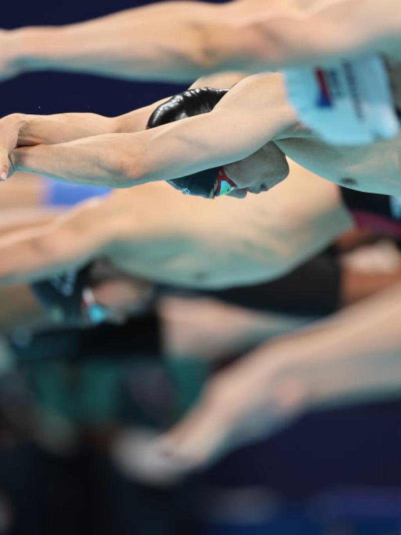 A group of male swimmers jumping into the pool at the start of a race