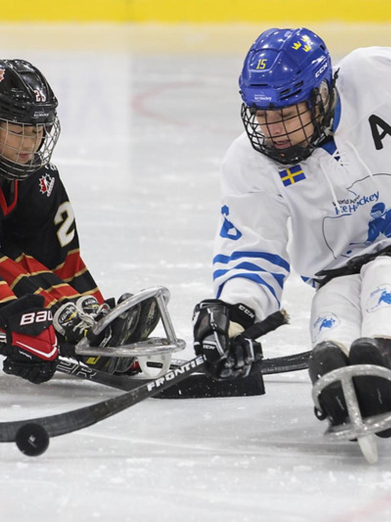 A Canadian player challenging a Team World player in a women's Para ice hockey game