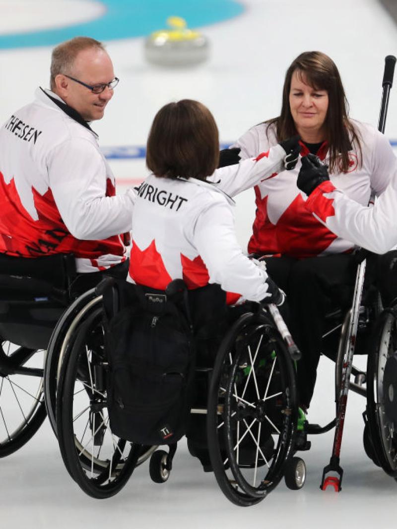 Four wheelchair curling athletes form a circle on the ice