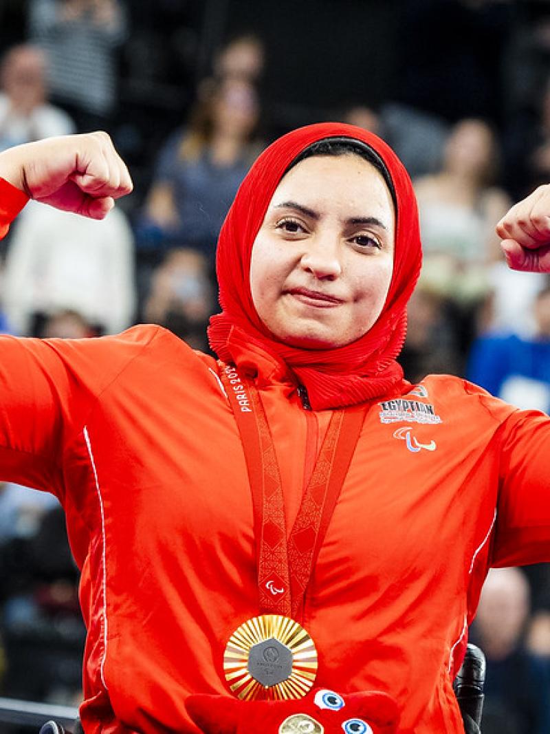 A female athlete with a gold medal flexing her arms 