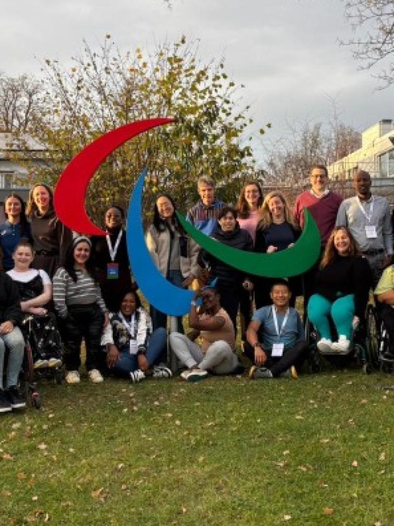 Twenty retired Para athletes take a photo in front of the Agitos symbol at the IPC Campus