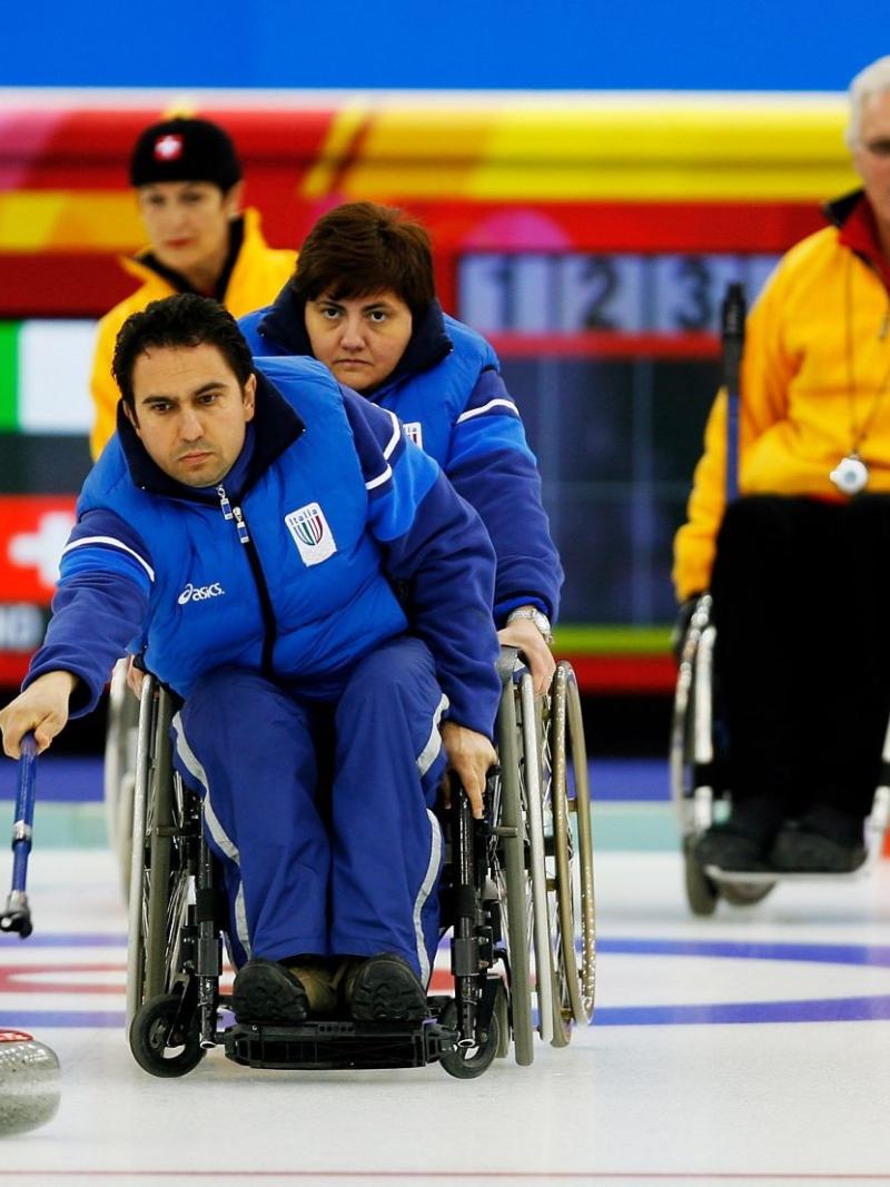 A male wheelchair curling athlete is delivering a stone with a stick during competition at Torino 2006.