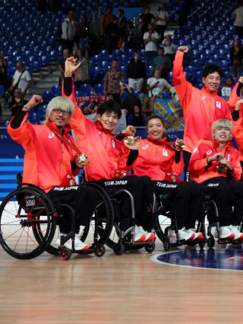 Eighteen wheelchair rugby players and officials wearing a red jersey pose for a photograph after receiving gold medals