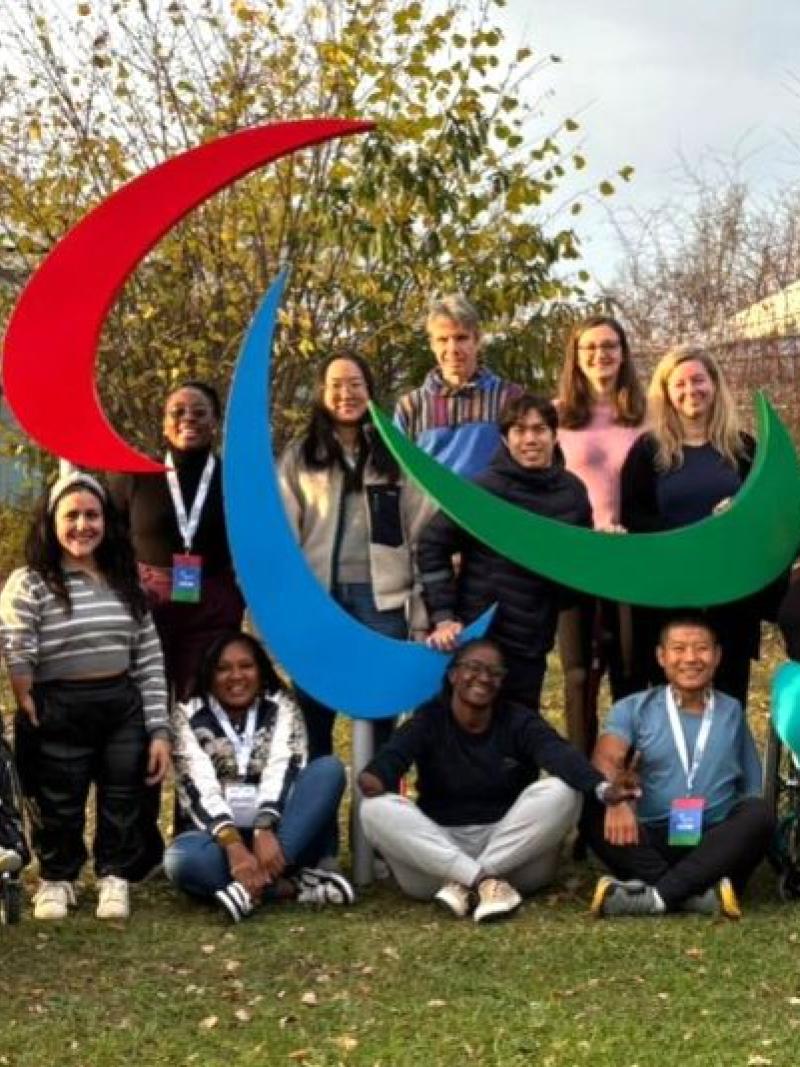 Twenty retired Para athletes take a photo in front of the Agitos symbol at the IPC Campus