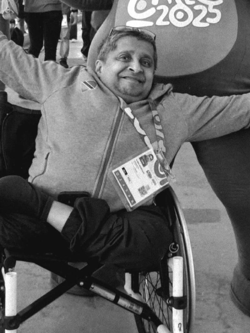A male official wearing an accreditation is opening his arms wide to pose for a photo