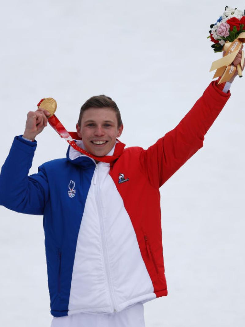 A male athlete wearing France's blue, white and red uniform celebrates on the podium at the Beijing 2022 Paralympics