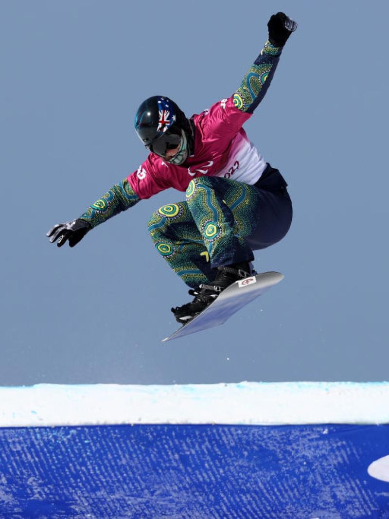 A male Para snowboard athlete is making a jump during the Beijing 2022 Paralympics