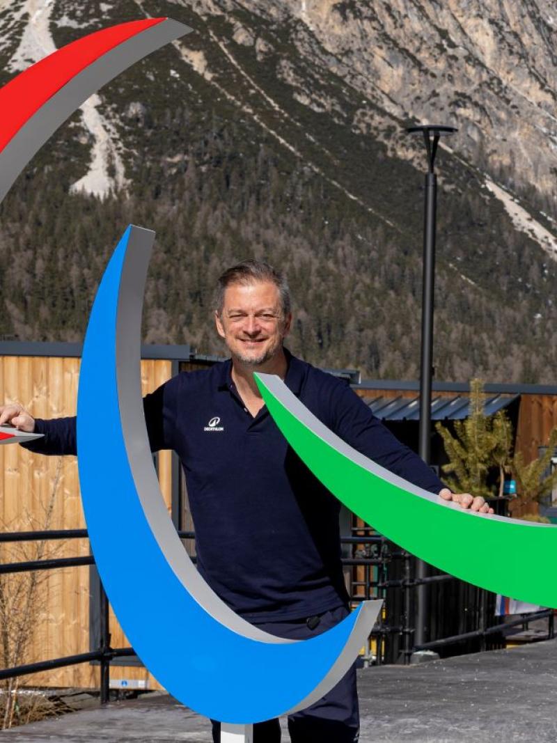 IPC President smiling at the camera next to the Agitos in the Paralympic village