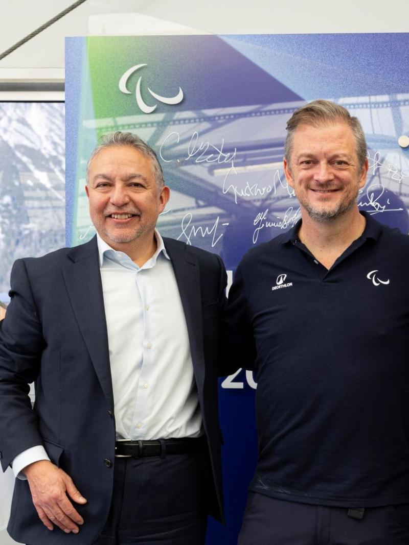 Three male officials are posing in front of a purple mural