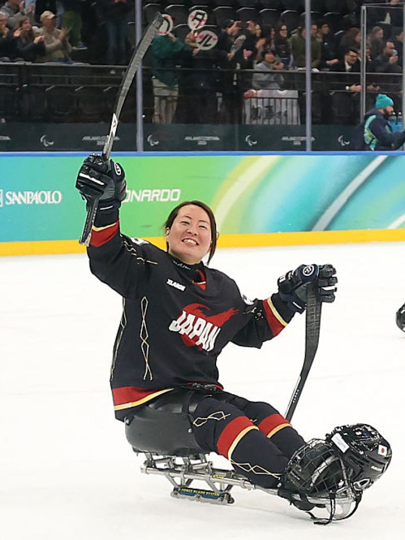 A female Para ice hockey player celebrates on the ice by raising her stick