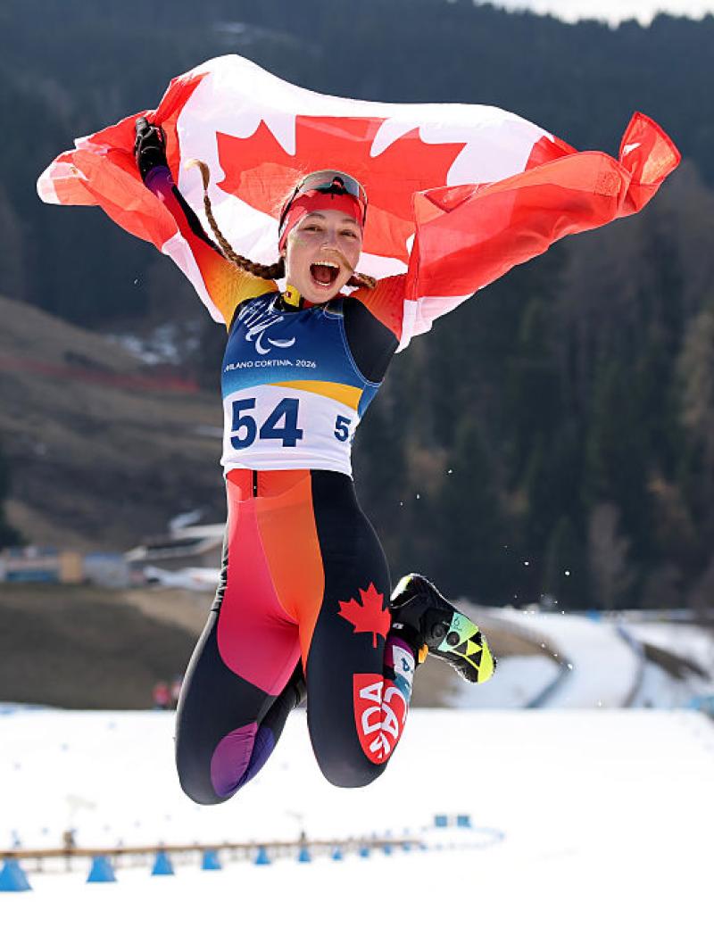 A female Paralympic skier is jumping while holding the Canadian flag