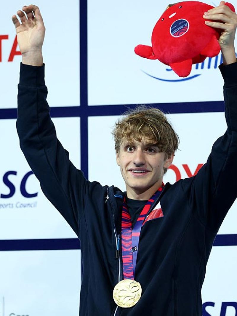 A young male athlete with open arms celebrating with a gold medal 