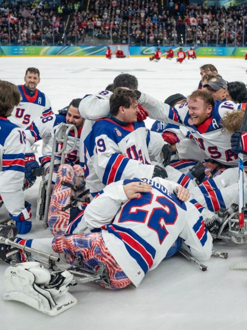 A group of Para ice hockey athletes from USA celebrate in the middle of a rink