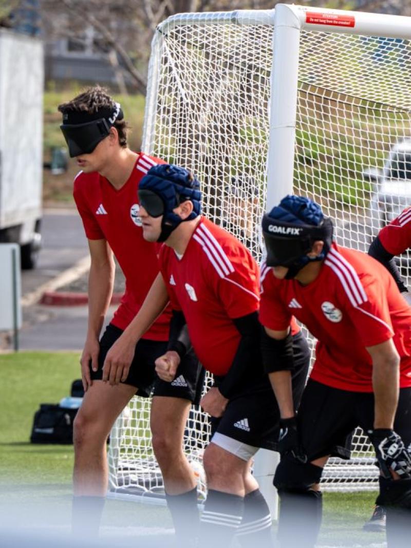 Four athletes wearing a red jersey are forming a line in front of the goal post