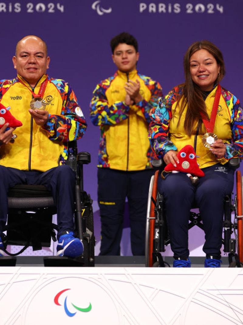 Male and female boccia athletes are on the podium, holding gold medals