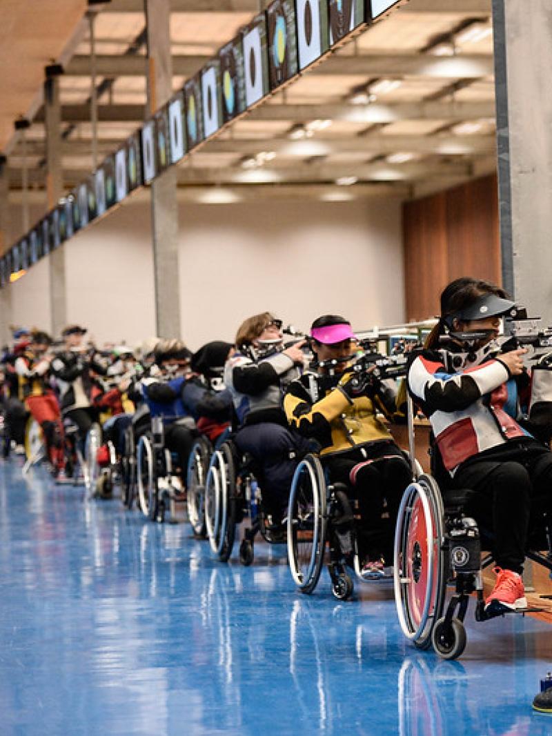 A group of female shooters in wheelchairs and one standing one in a shooting range