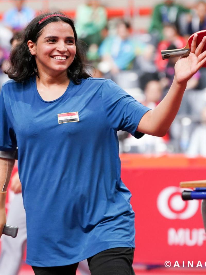 A female Para table tennis player smiles while holding a raquet