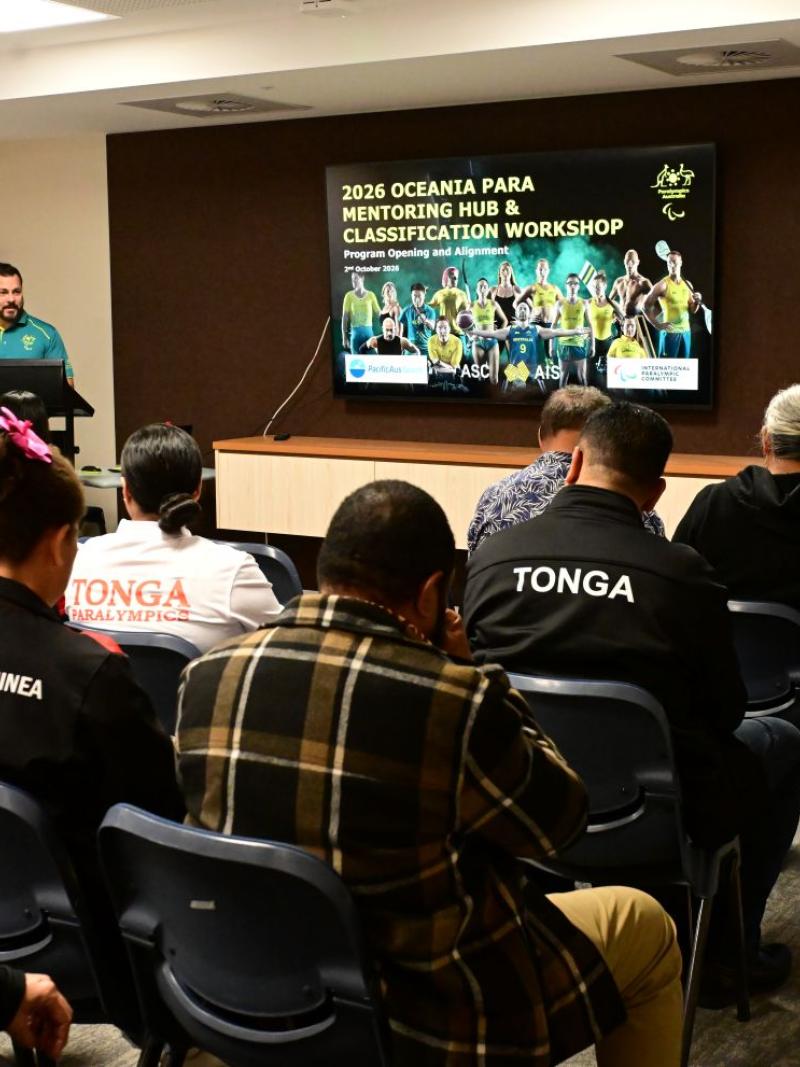 A male official is making a presentation in front of around 10 participants
