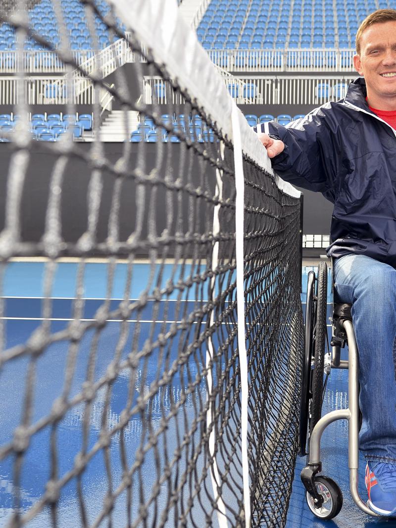 A picture of an athlete in a wheelchair next to a tennis let.