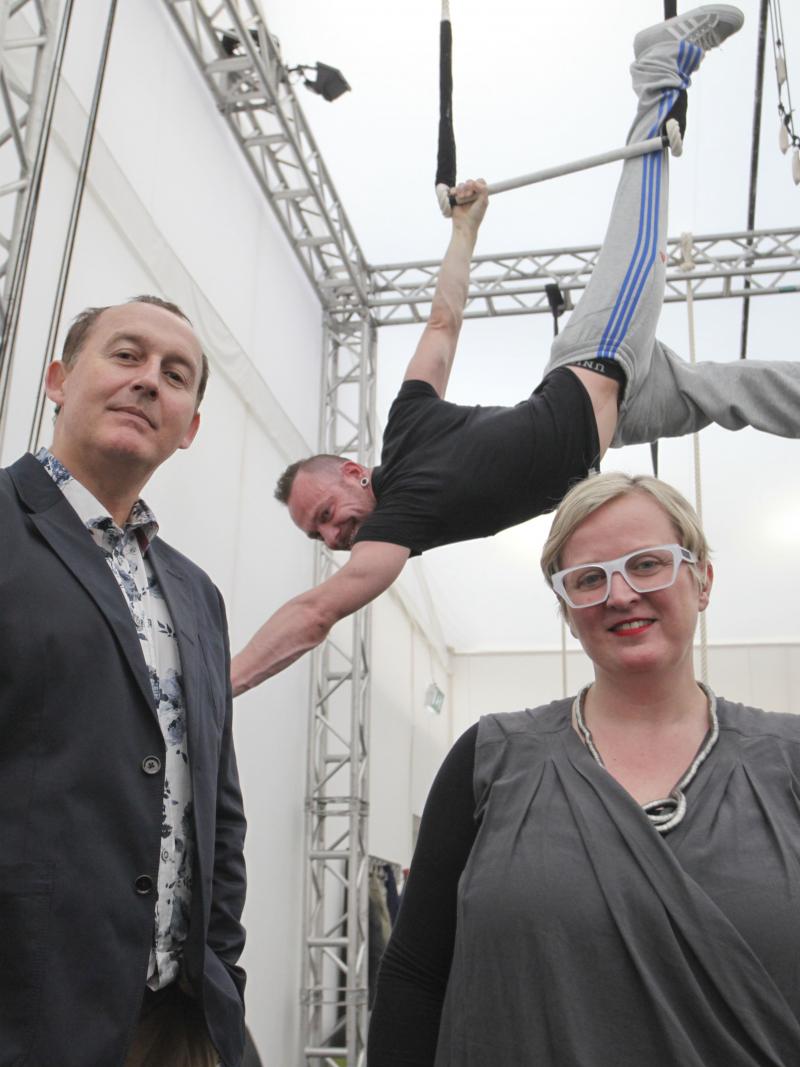 A picture of two person standing and one rapeze artist.