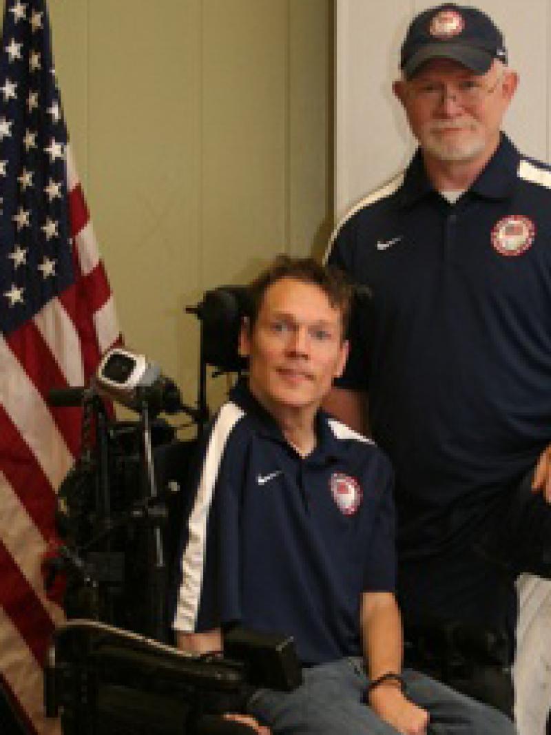 A picture of a man in an electric wheelchair posing for a picture with another man