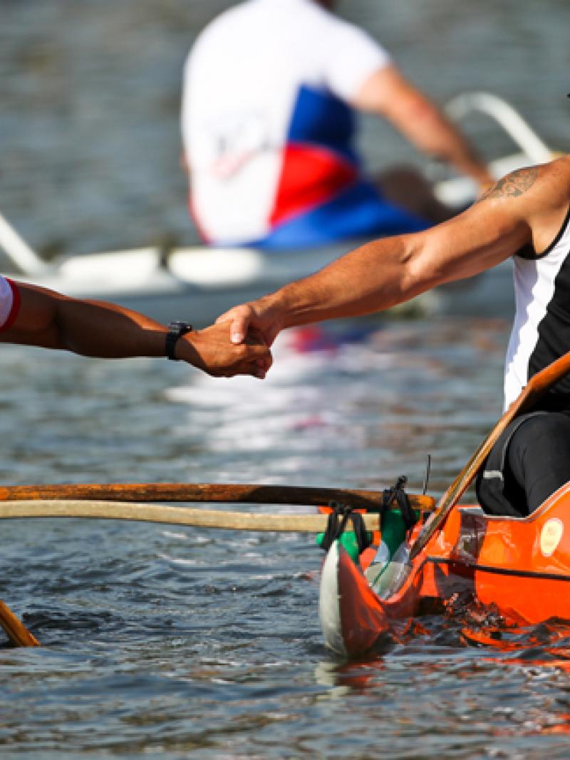 A picture of 2 men in a canoe shaking their hands celebrating a victory