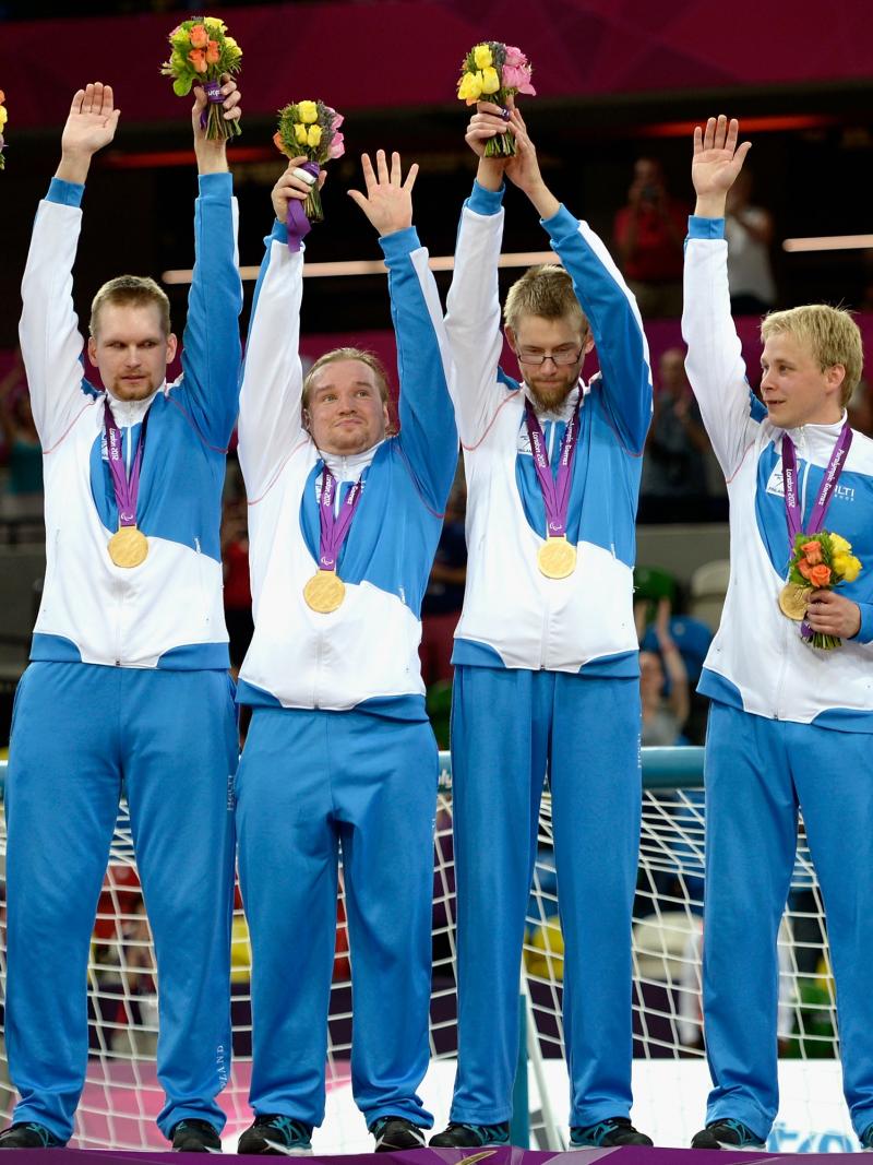 Six men in training suits standing in a row, waving and celebrating