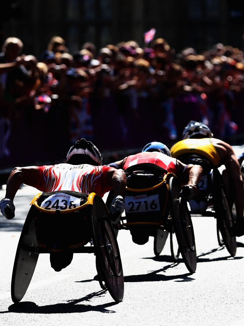 group of men in racing wheelchairs pass spectators